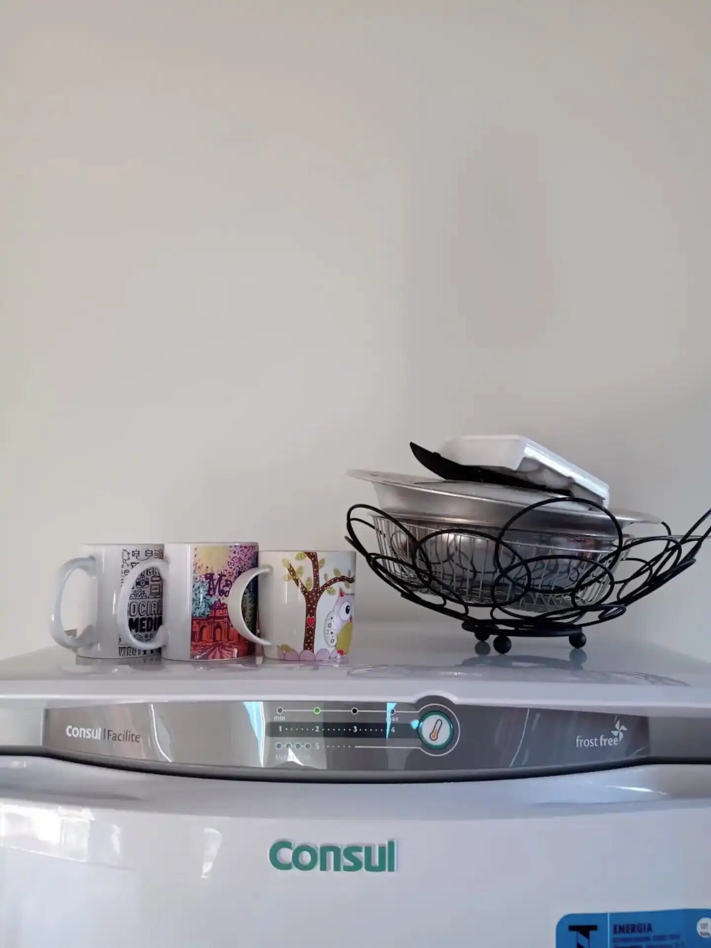 A coffee maker with three mugs on top, a basket with a plate, and a digital display.
