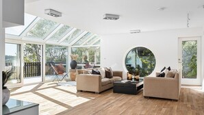 A modern living room with a large round mirror, two sofas, a coffee table, and a glass door leading to an outdoor area.