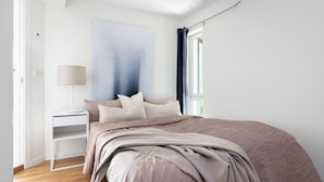 A bedroom with a bed, a bedside table, a lamp, and a window with curtains.