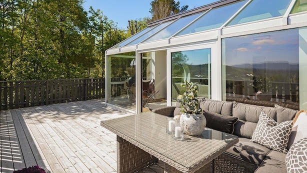 A modern outdoor patio with a glass-enclosed seating area, wicker furniture, and a wooden deck.
