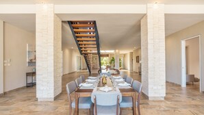 A spacious dining area with a long table set for six, flanked by two white brick pillars, leading to a staircase.
