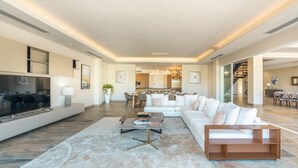 A spacious living room with a large flat-screen TV, a white sofa, and a coffee table.