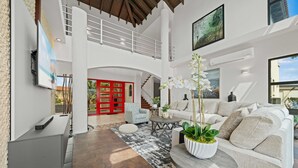 A spacious living area with a high ceiling, a staircase, a white sofa, a coffee table, and a potted plant. - Caya di Sero 18 Tierra del Sol (Noord)