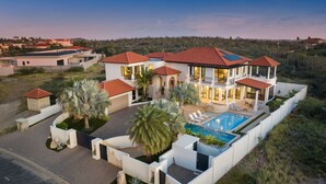 A large, modern house with multiple sections, a swimming pool, and a well-maintained garden. - Caya di Sero 18 Tierra del Sol (Noord)
