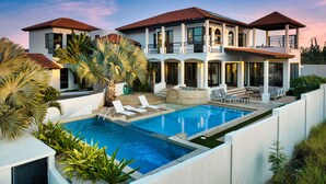 A modern two-story house with a swimming pool, outdoor seating, and a large palm tree. - Caya di Sero 18 Tierra del Sol (Noord)