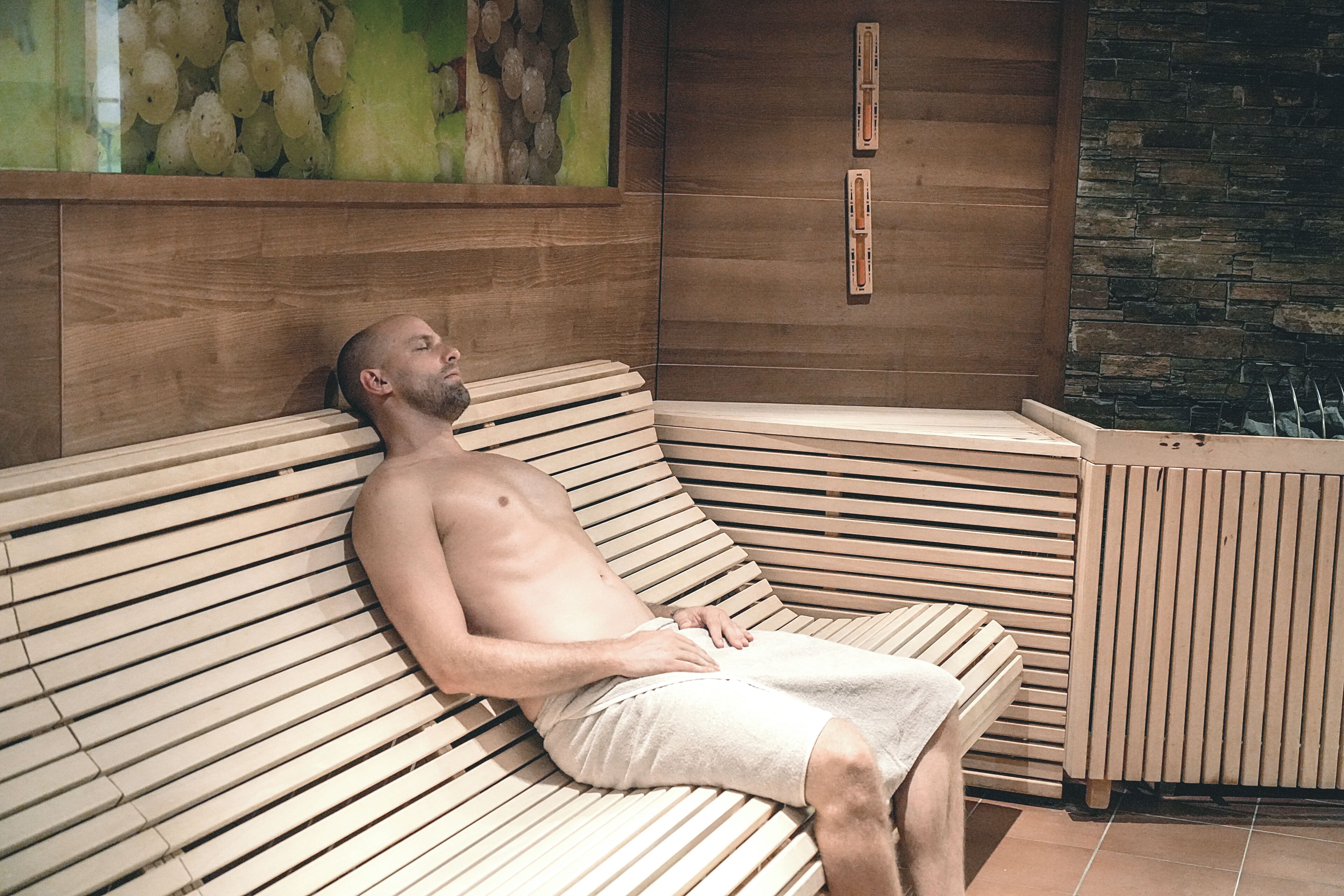A man lying on a wooden bench with slats, in a room with a stone wall and a wooden panel.