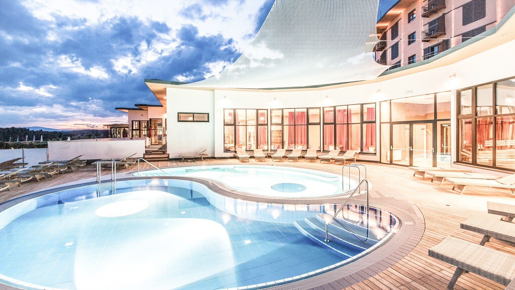 Un hotel moderno con piscina, tumbonas y vistas a la ciudad.