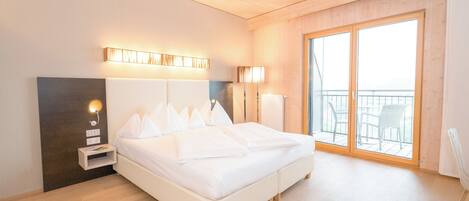 Un dormitorio moderno con una cama grande, lámparas de noche, una mesita de noche y vistas al exterior a través de una puerta corrediza de vidrio.