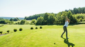 Un campo de golf con cielo despejado, césped bien cuidado y árboles al fondo.