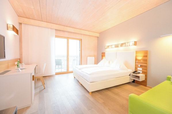Hotellihuone, jossa on sänky, työpöytä, tuoli, yöpöytä ja vihreä sohva.