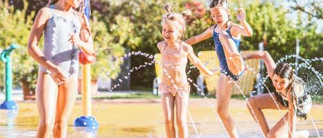 Niños jugando en un parque acuático con chorros de agua.