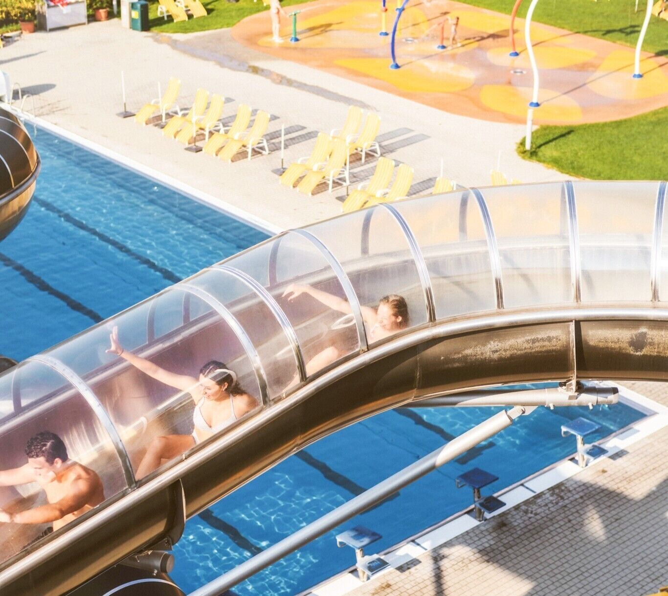 A water slide with clear sections, a pool, and lounge chairs.