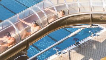 A water slide with people sliding down into a pool area, surrounded by sun loungers and a water park.