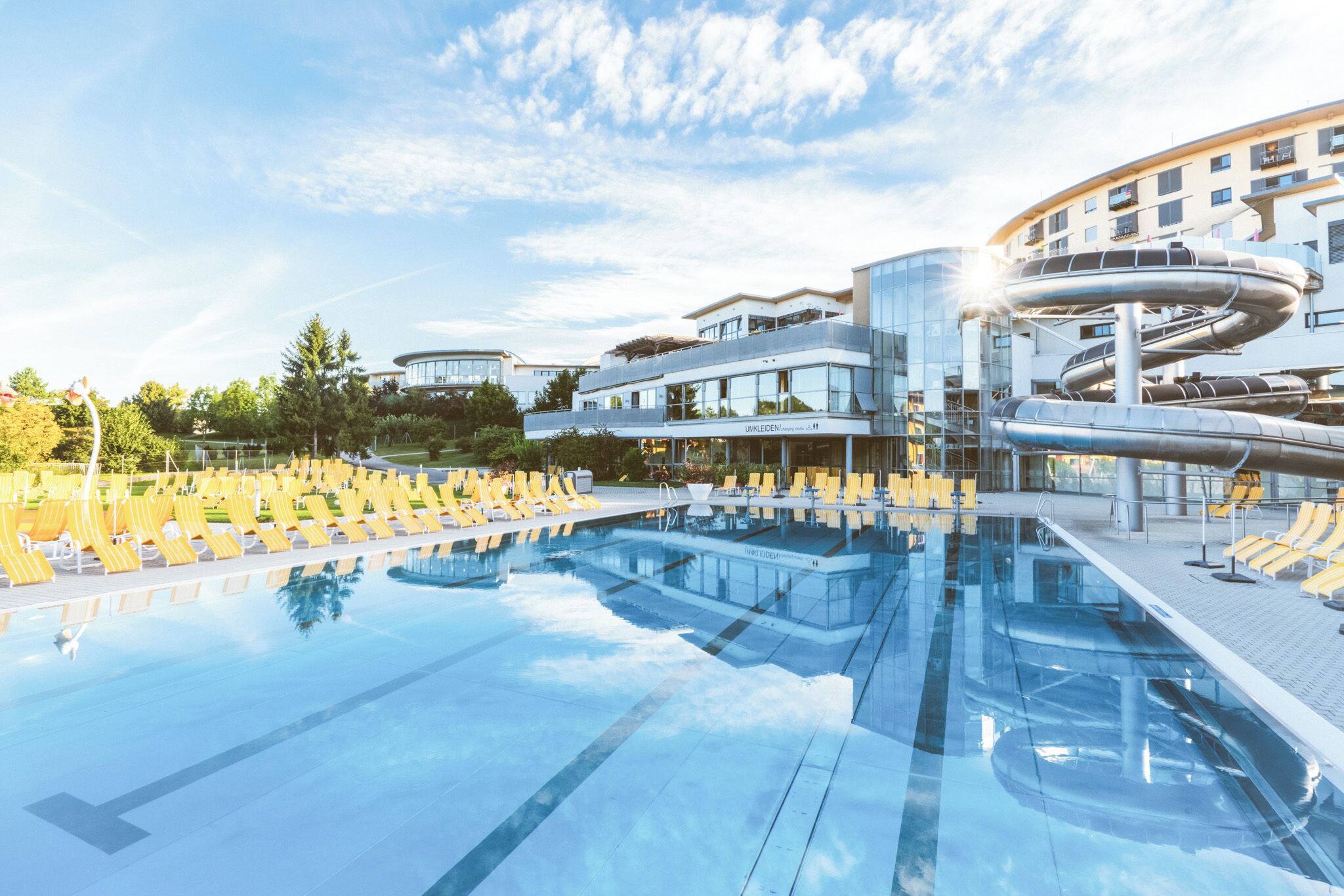 A modern hotel with a large outdoor swimming pool, yellow lounge chairs, and contemporary architecture.