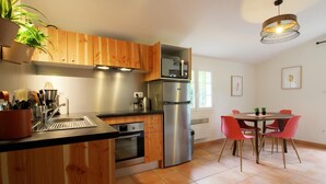 A modern kitchen with wooden cabinets, stainless steel appliances, and a dining area with red chairs. - DOMAINE DU FLAMAND - Gîte JUNCA  (Naujac-sur-Mer)