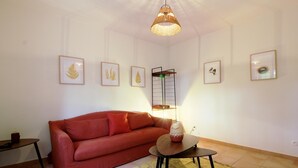 A living room with a red sofa, a small table with a lamp, and framed artwork on the walls. - DOMAINE DU FLAMAND - Gîte JUNCA  (Naujac-sur-Mer)