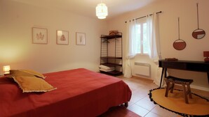 A bedroom with a bed, a desk, a chair, a radiator, and a window with curtains. - DOMAINE DU FLAMAND - Gîte JUNCA  (Naujac-sur-Mer)