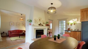 A modern living room with a fireplace, a dining area with a round table, and a kitchen with wooden cabinets. - DOMAINE DU FLAMAND - Gîte JUNCA  (Naujac-sur-Mer)