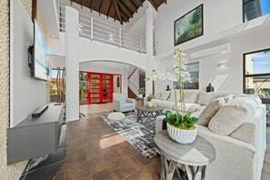 A spacious living area with a high ceiling, a staircase, and a view of the outdoors.