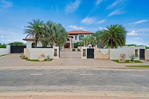 A modern two-story house with a red-tiled roof, a gated driveway, and palm trees. - Lux Villa Oasis: 5BR w Pool* Playground near Beach (Noord)