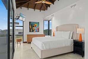A bedroom with a large bed, a ceiling fan, a TV, and a painting on the wall. - Lux Villa Oasis: 5BR w Pool* Playground near Beach (Noord)
