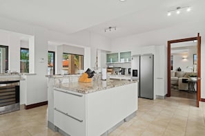 A modern kitchen with white cabinetry, a granite countertop, and a built-in island with a knife block. - Lux Villa Oasis: 5BR w Pool* Playground near Beach (Noord)