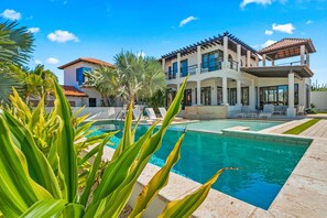 A modern two-story house with a swimming pool, surrounded by tropical plants.