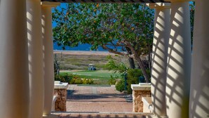 A covered walkway leading to a view of a golf course with a body of water in the background. - Lux Villa Oasis: 5BR w Pool* Playground near Beach (Noord)