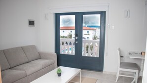 Una sala de estar con un sofá, una mesa de centro y un sillón. Se ve una puerta con vistas al exterior.