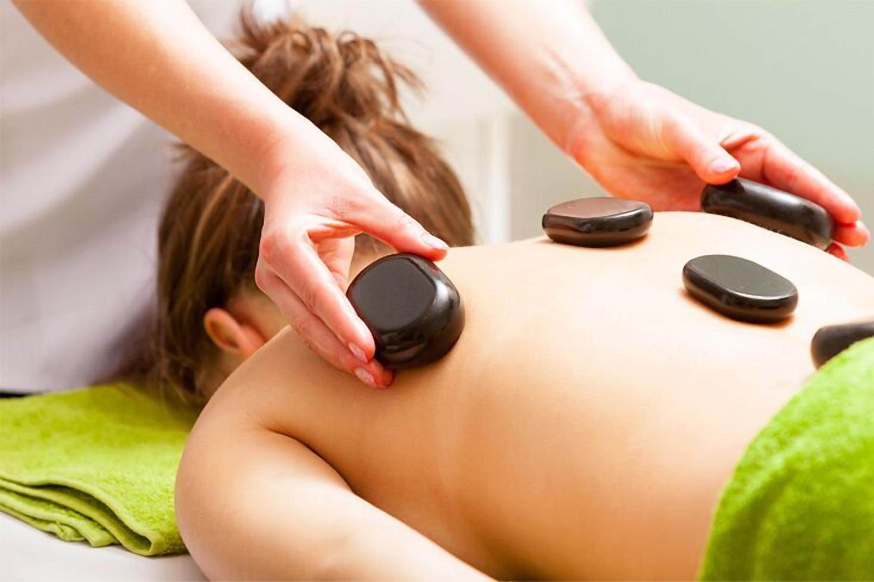 A person receiving a massage with a green towel and black stones on their back.