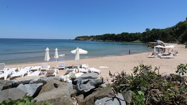 A beach with white lounge chairs and umbrellas, rocky foreground, and a clear blue sky. - Menada Vris Apartments (Tsarevo)