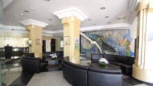 A lobby with a reception desk, black leather sofas, a staircase, and a mural on the wall. - Menada Vris Apartments (Tsarevo)