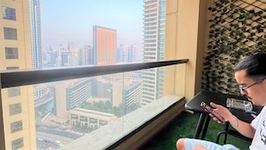 Un balcone con vista sulla città, un tavolo e una persona che usa uno smartphone.