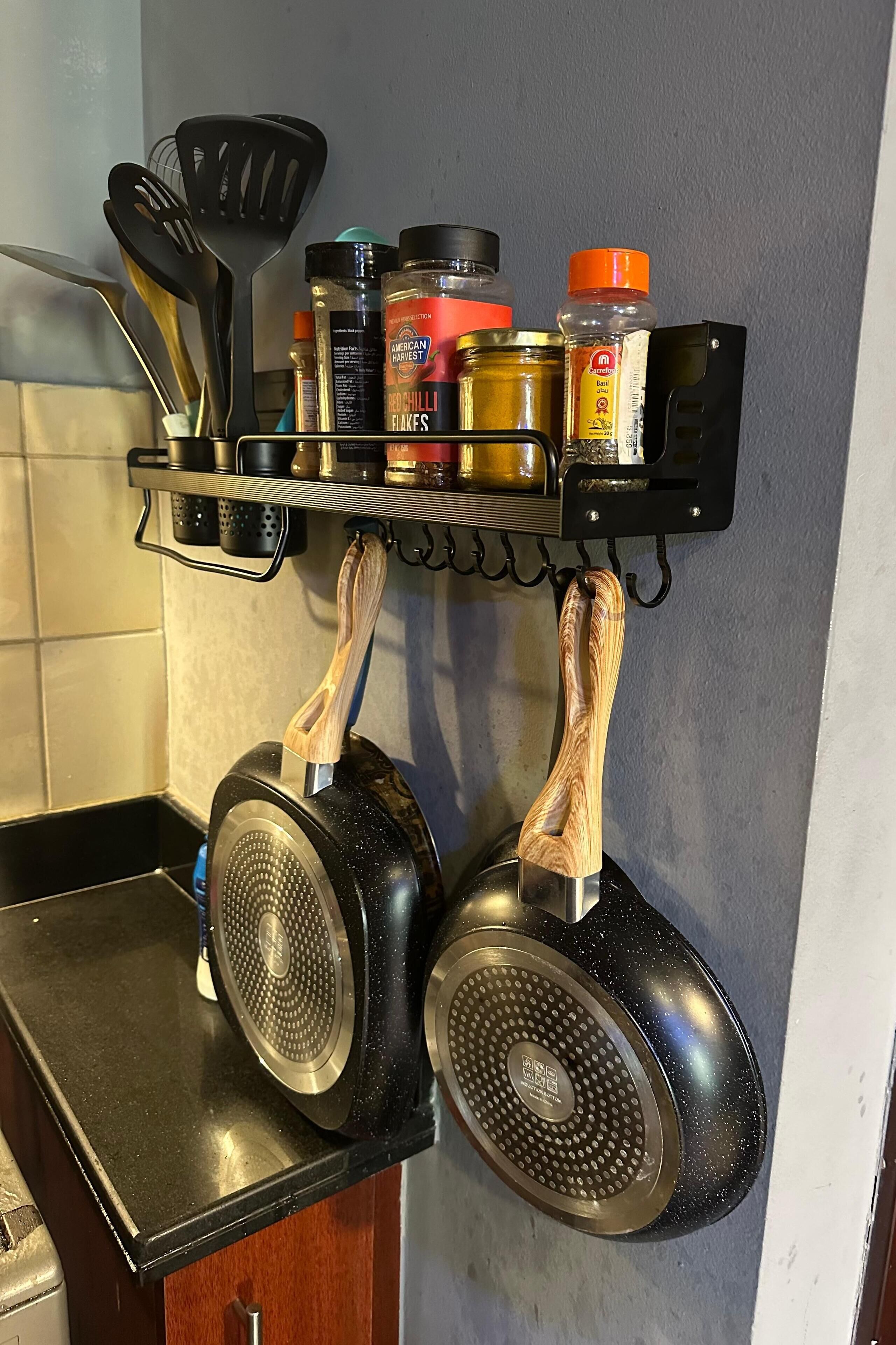 A kitchen with two hanging pans, a spice rack with various jars, and a set of utensils.