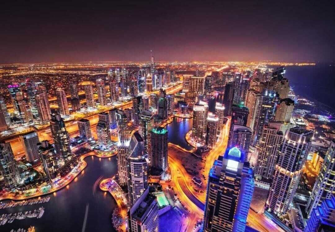Une vue nocturne d’une ville, avec ses gratte-ciel, une rivière et un pont.