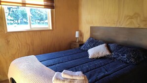 Un lit bien fait, avec une couette bleue, un oreiller blanc et une couverture beige.