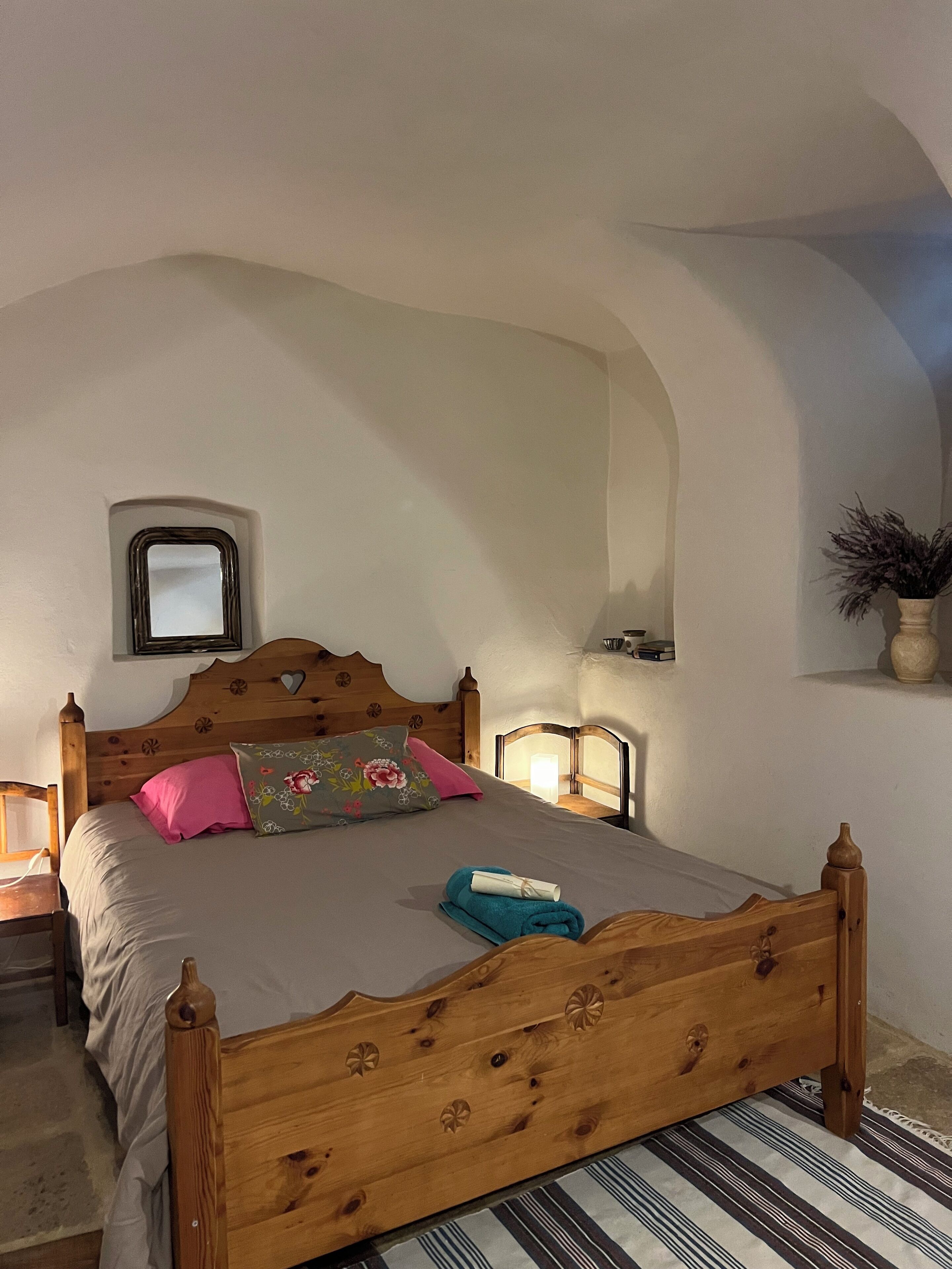 Une chambre à coucher avec un lit en bois, une table de chevet, un miroir et une étagère murale agrémentée d’une plante.