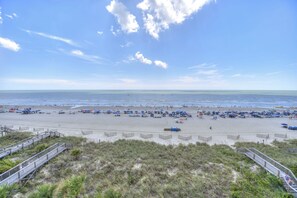 A beach with a wooden boardwalk leading to the shore, a lifeguard tower, and umbrellas on the sand. - Spacious Oceanfront 3BR 3BA at Crescent Shores - Pools, Lazy River & Stunning Views (North Myrtle Beach)