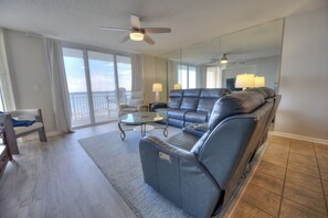 A modern living room with a leather sofa, a glass coffee table, and a balcony with a view. - Spacious Oceanfront 3BR 3BA at Crescent Shores - Pools, Lazy River & Stunning Views (North Myrtle Beach)