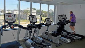 Une salle de sport équipée de tapis de course et d’appareils elliptiques, dotée de grandes fenêtres et offrant une vue sur les maisons environnantes.