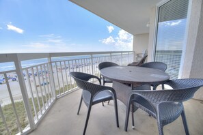 A balcony with a table and chairs, overlooking a beach with umbrellas and people.