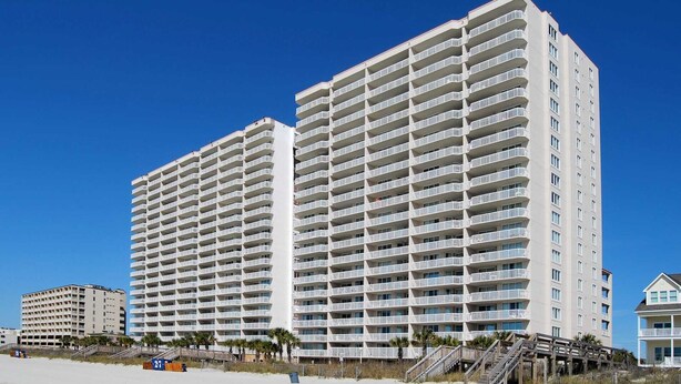 Un hôtel de grande hauteur doté de nombreux balcons, situé près d’une plage.