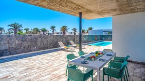Une terrasse extérieure avec une piscine, un mur en pierre et une table dressée pour le repas.