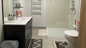 A modern bathroom with a shower, toilet, and sink. There are two rugs on the floor, a trash bin, and a mirror with shelves above the sink. - Beautiful, quiet studio near Vichy (Saint-Rémy-en-Rollat)