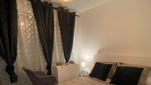 A bedroom with a bed, a chair, a bedside table, a lamp, and a window with curtains. - Beautiful, quiet studio near Vichy (Saint-Rémy-en-Rollat)