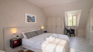 Une chambre à coucher comprenant un lit, une table de chevet, une lampe, un tableau, une armoire, une fenêtre et une chaise.