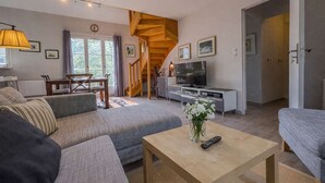 Un salon avec un canapé, une table basse ornée d’un vase, un téléviseur et un escalier.