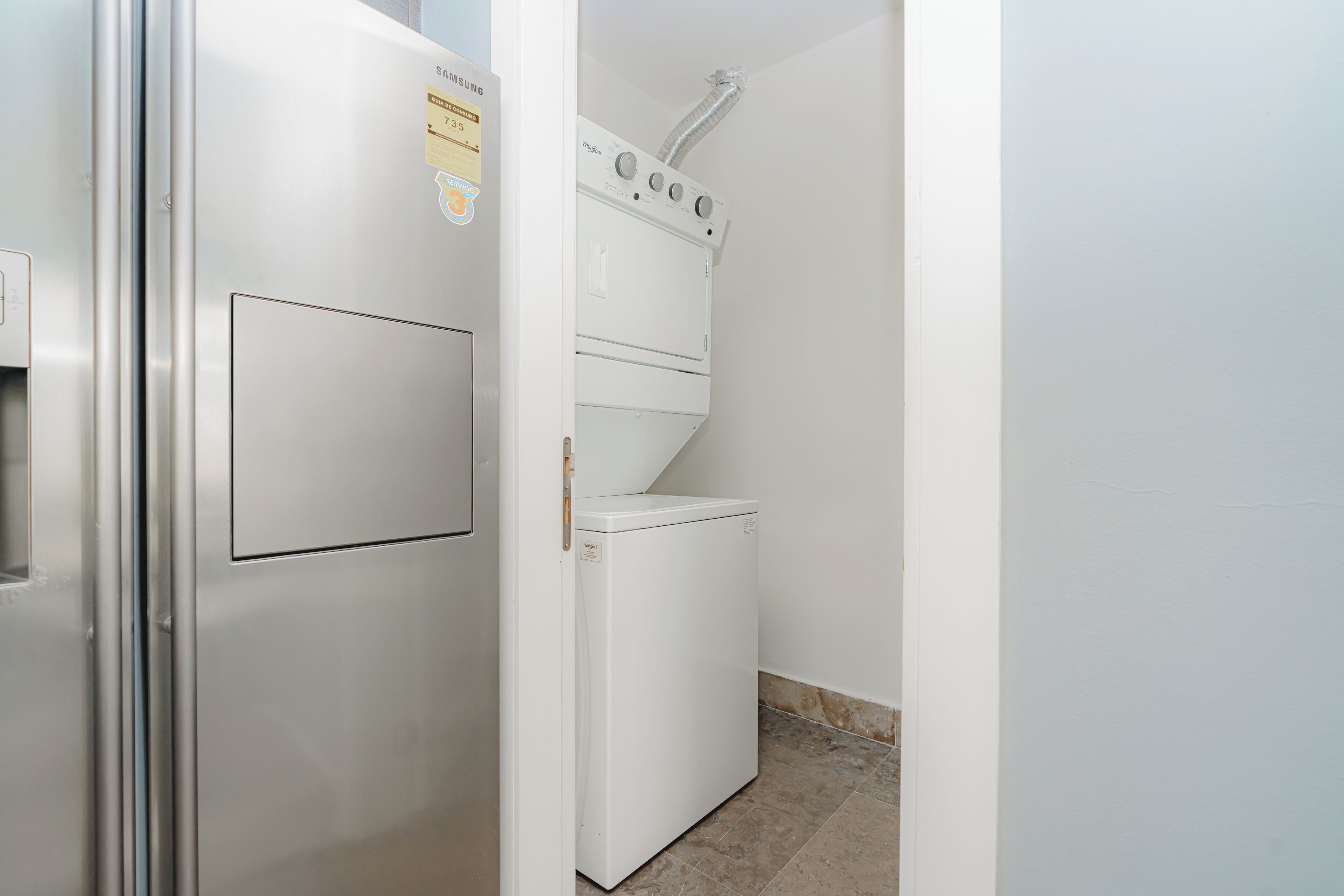 Un lavadero pequeño con un refrigerador de acero inoxidable, una lavadora y una secadora.