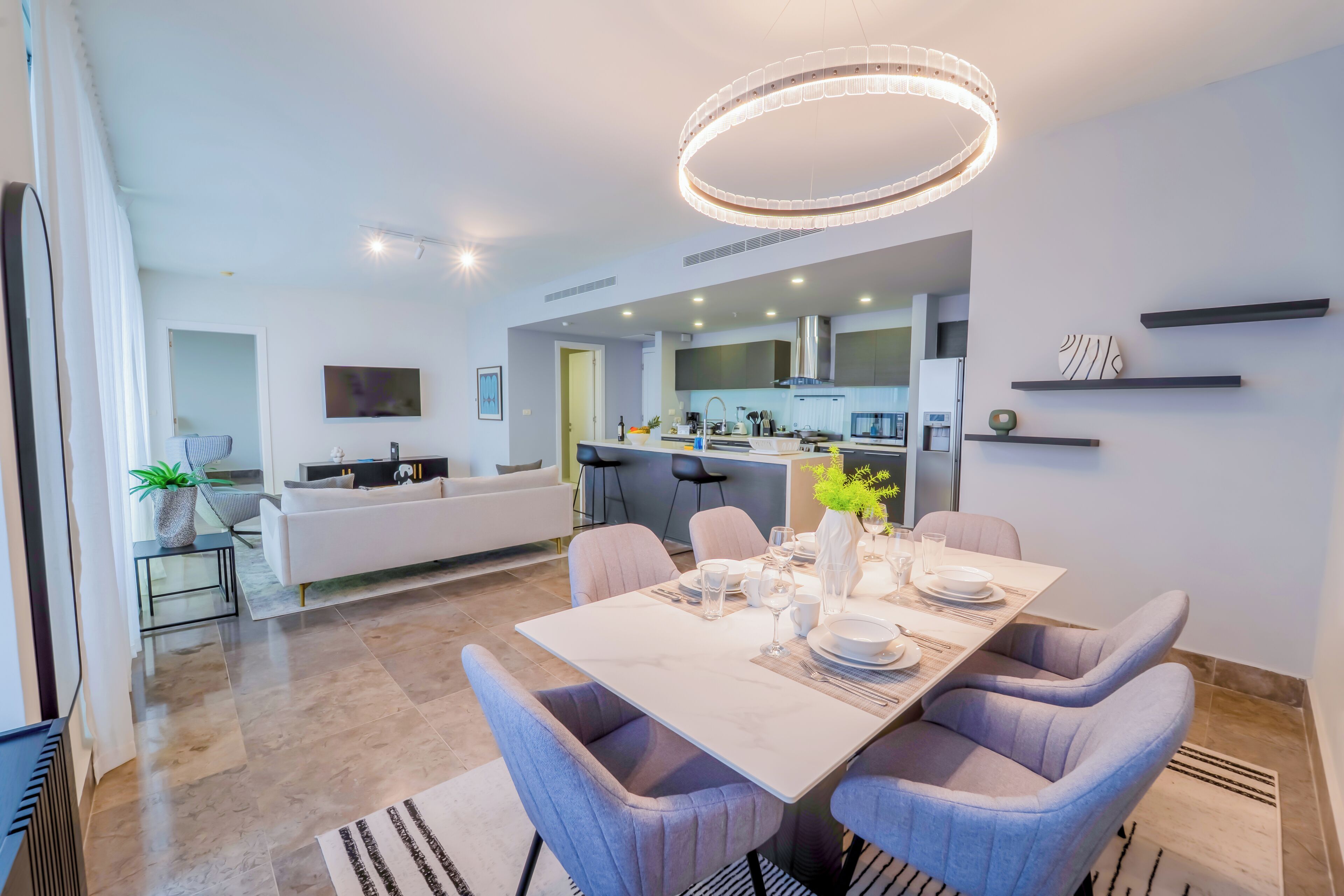 A modern dining area with a marble table, grey upholstered chairs, and a contemporary chandelier.