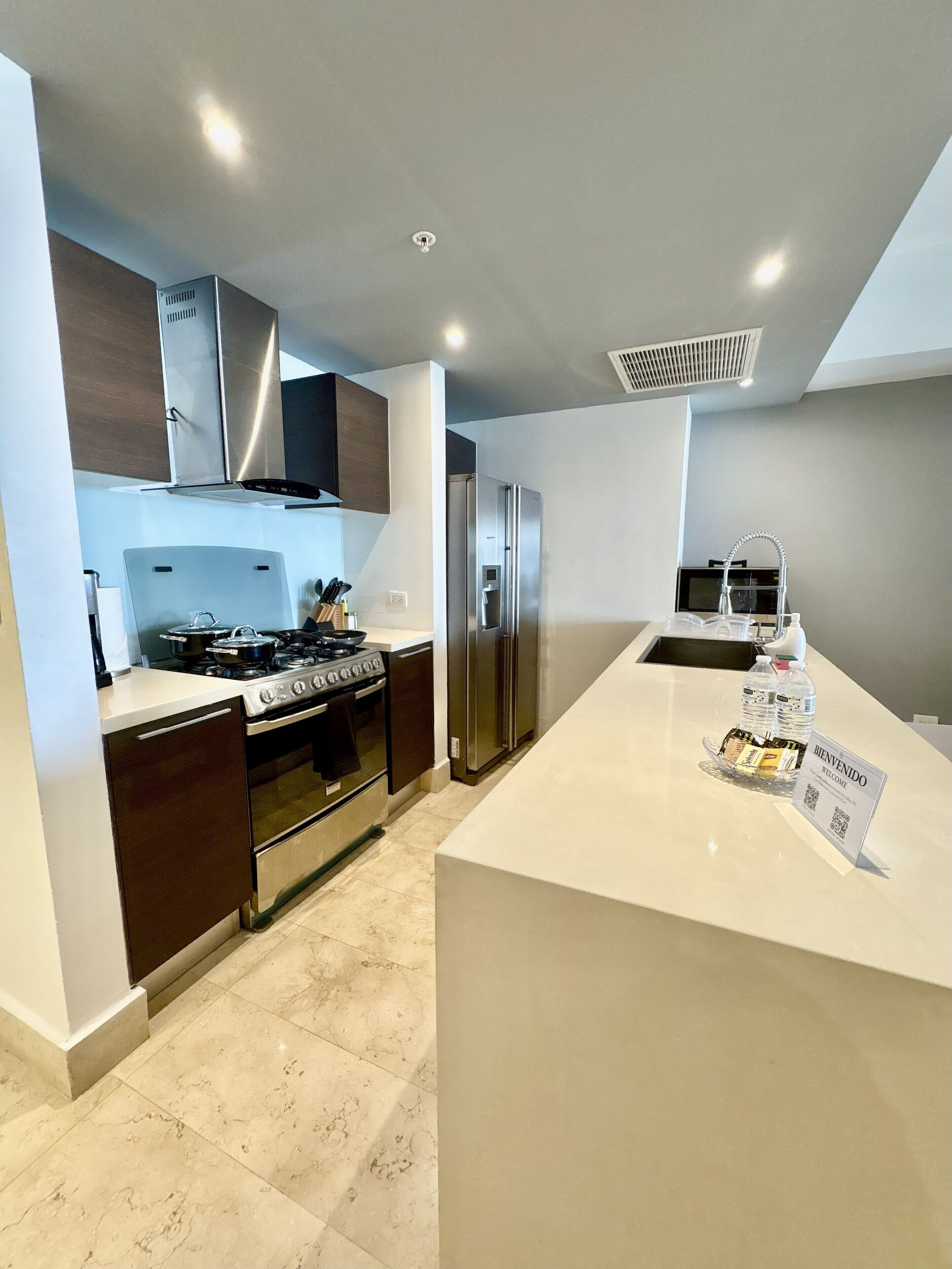 Een moderne keuken met een centraal eiland, roestvrijstalen apparatuur en een welkomstbord.